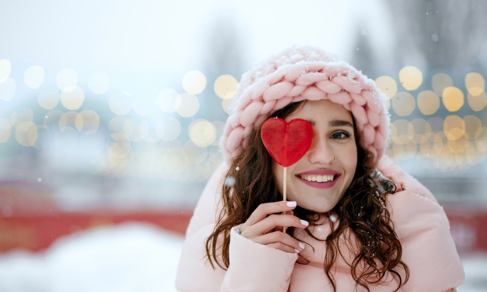 Dziewczyna w różowym stroju zimowym z lizakiem w kształcie serca przy oku